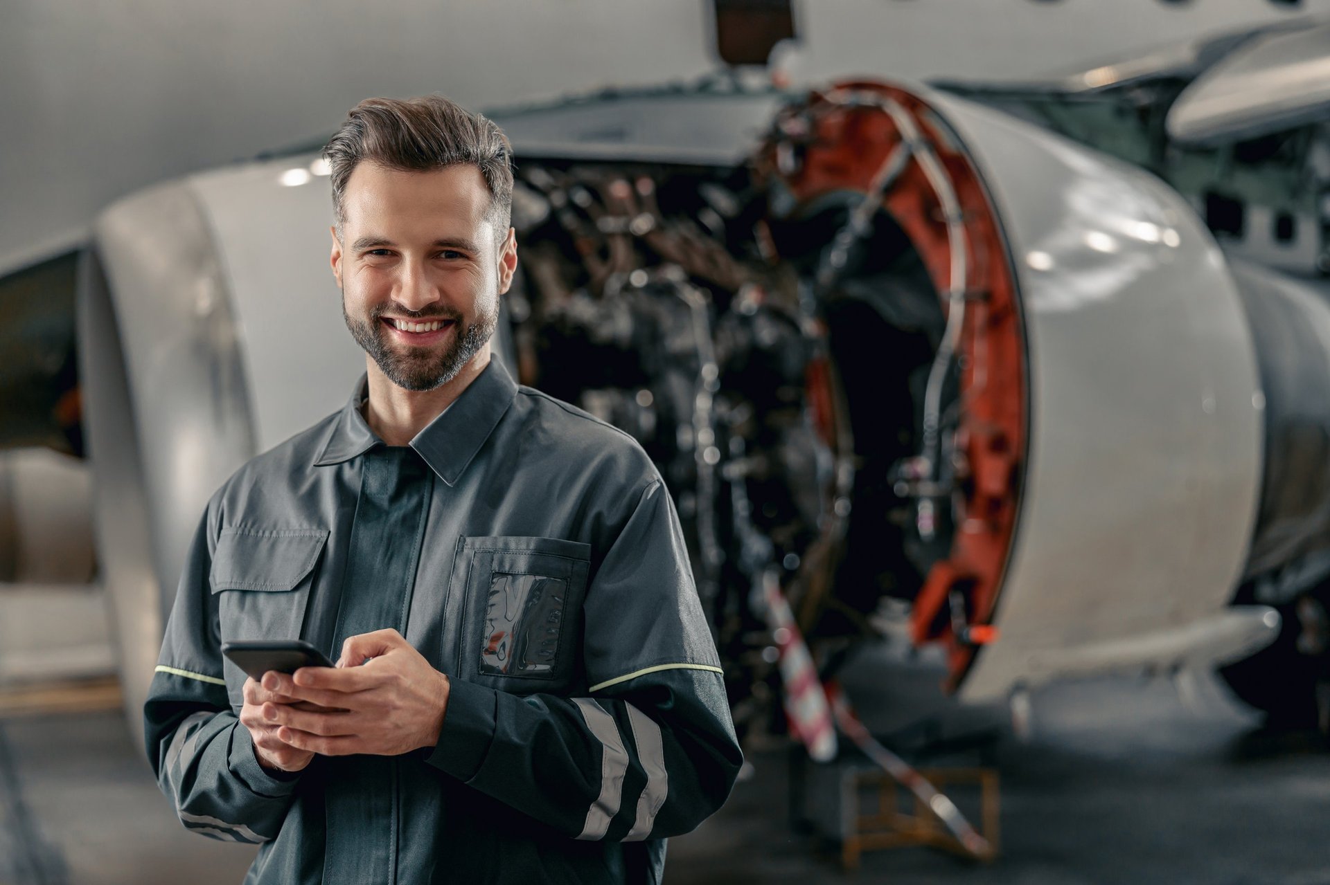 Smiling Ghanaian aircraft maintenance technician holding smartphone in hangar