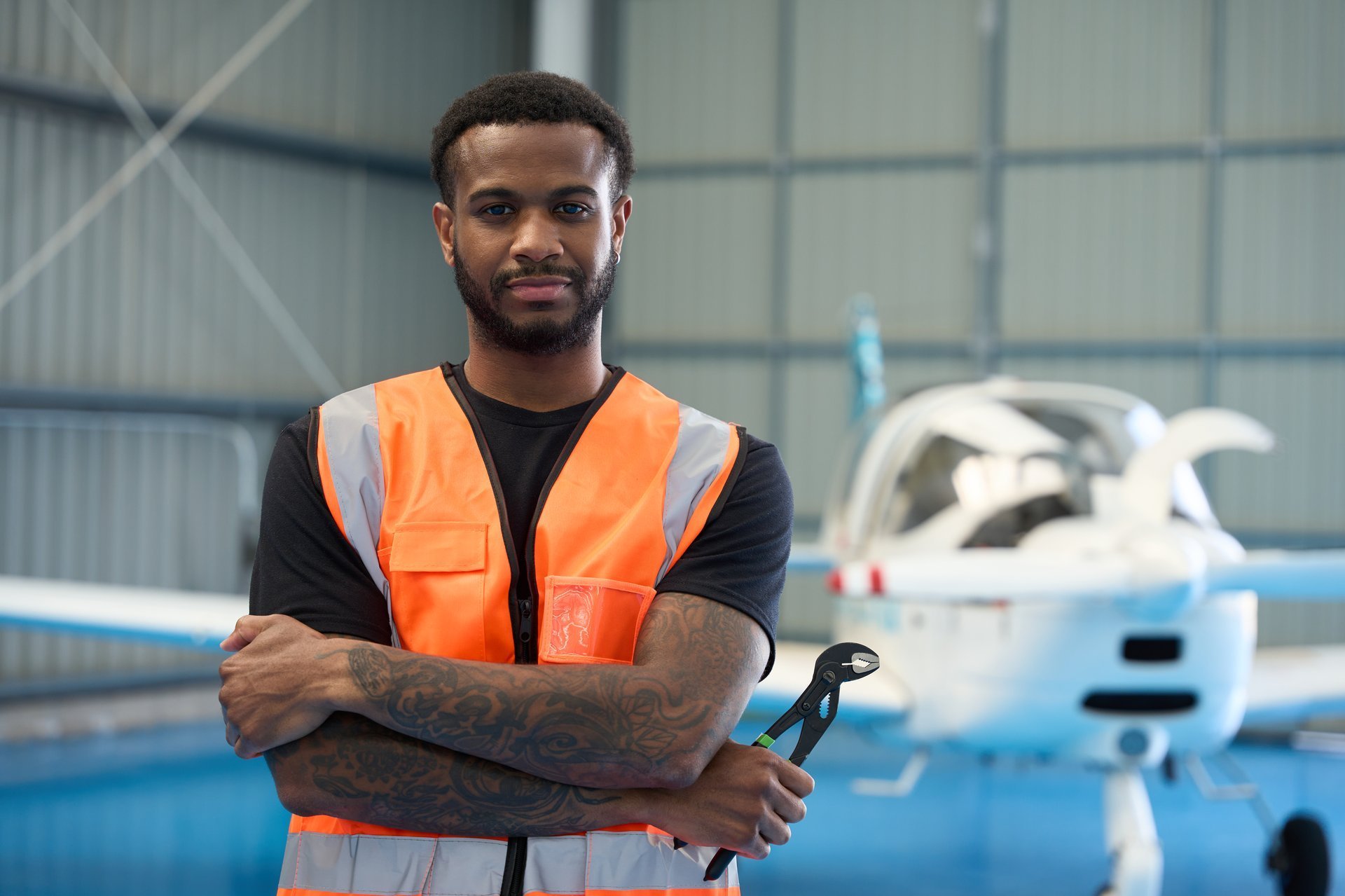 Confident Ghanaian aircraft mechanic holding tools in hangar with airplane in background