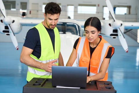 Two aircraft mechanics collaborating on laptop for maintenance checks