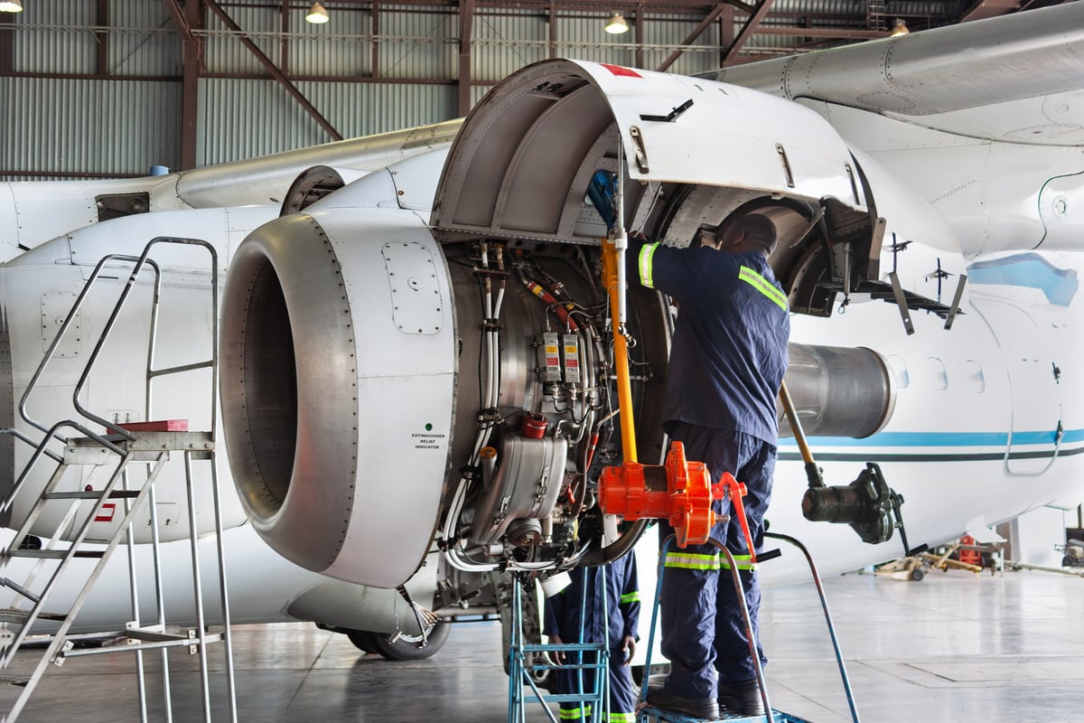 Two plane technicians working on open turboprop airplane engine during mechanical inspection inside hangar